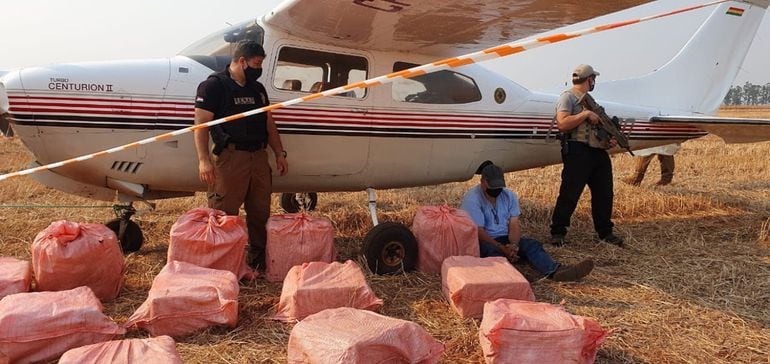 El piloto Carlos Cuéllar junto con la carga de 400 kilogramos de cocaína y la avioneta.