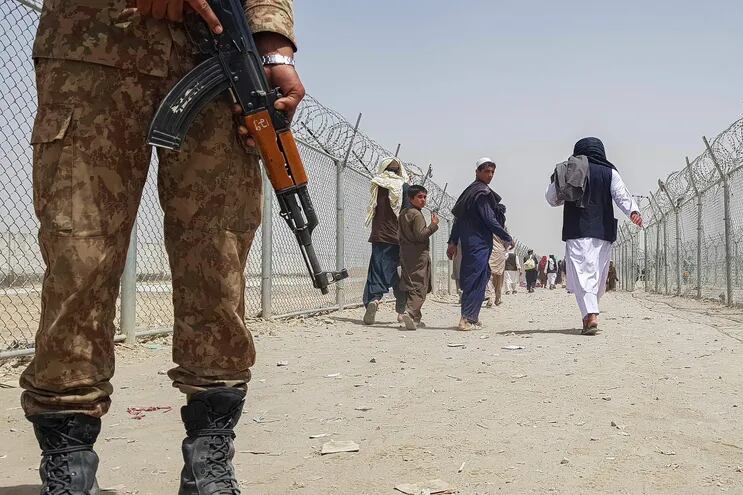 Un soldado pakistaní monta guardia mientras que un grupo de afganos retorna a su país en un cruce de frontera.