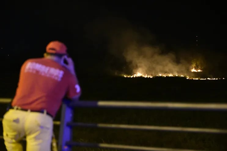 Bomberos apostados en la costanera veridican desde lejos las labores de sus camaradas en combate a las llamas.