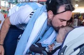Tomás Centurión da un beso en la frente a su hijo de 5 meses Mirko que lo recibió en la Estación de Buses de Asunción este viernes.