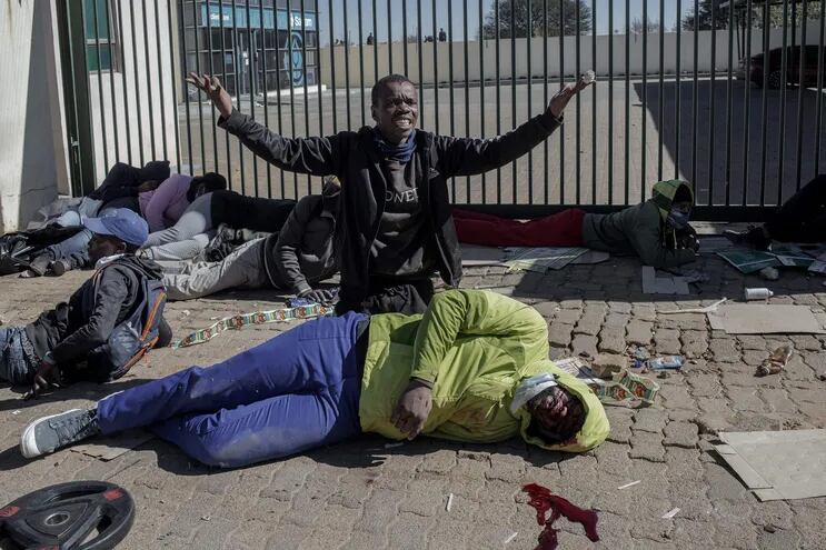 Un supuesto saqueador gesticula ante miembros de la Fuerza Nacional de Defensa de Sudáfrica (que no se ven en la foto) y a quienes les pide ayuda para el hombre que yace herido en el piso.