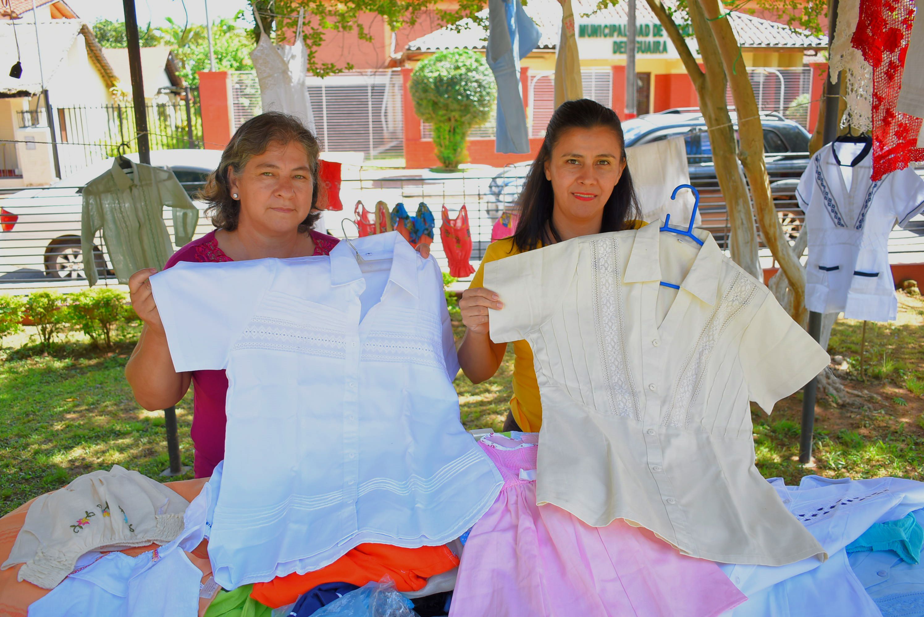 Las artesanas Mirtha Cardozo y Teresa Leiva exhibiendo hermosas blusas que pueden adquirirse en la Expo Ao Po'i a tan solo G. 150 mil.