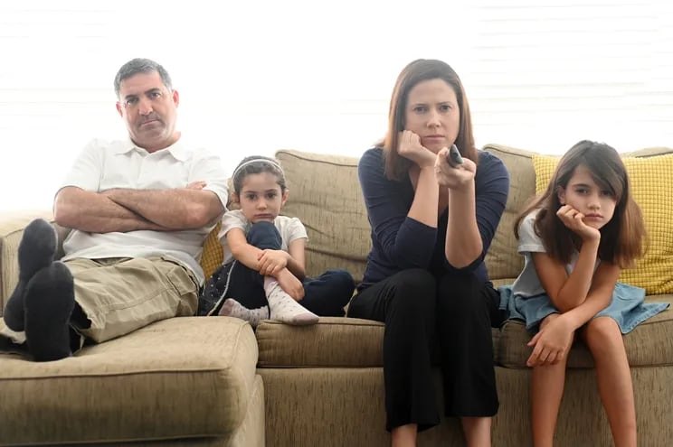 Un papá, dos hijas y una mamá sentados en un sillón, con cara de aburridos y enojados.