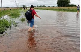 Una docente cruza a pie en la zona de Tacuara´i del distrito de Tacuaras para llegar a la ruta PY04 luego de que el vehículo que lo transportaba quedara atascado en el camino en medio del agua.