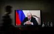 Una mujer camina frente a una pantalla de TV que muestra al presidente ruso Vladimir Putin.