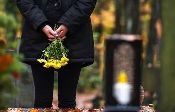 viuda frente a una tumba en el cementerio, con un ramo de flores amarillas en las manos