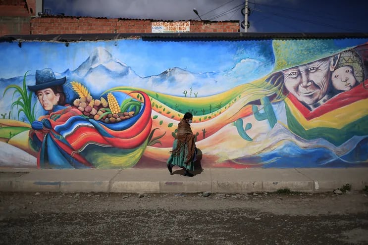 Una mujer indígena camina frente a un mural en la zona de Senkata en El Alto, Bolivia el 23 de marzo de 2021, donde se produjeron enfrentamientos entre simpatizantes y opositores del expresidente boliviano Evo Morales que terminaron con su renuncia en noviembre de 2019.