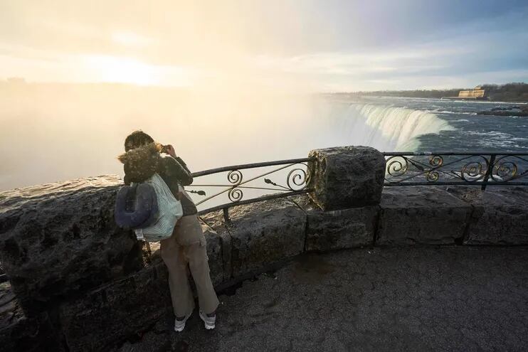 Una persona toma una fotografía mientras el sol sale sobre las Cataratas Horseshoe en las Cataratas del Niágara, Ontario, Canadá.