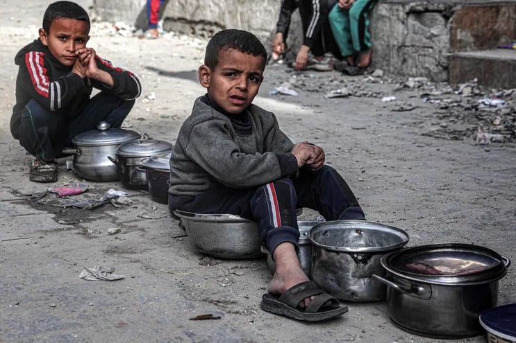 Niños con recipientes para comida forman fila para recibir alimentos en Gaza.
