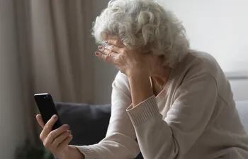Una mujer de la tercera edad con el pelo canoso mira su teléfono con preocupación.