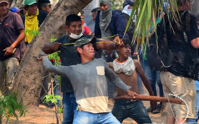 Un hombre arroja una piedra y otro tensa una hondita durante las protestas frente al Congreso contra el aumento de las penas a los invasores de propiedades.