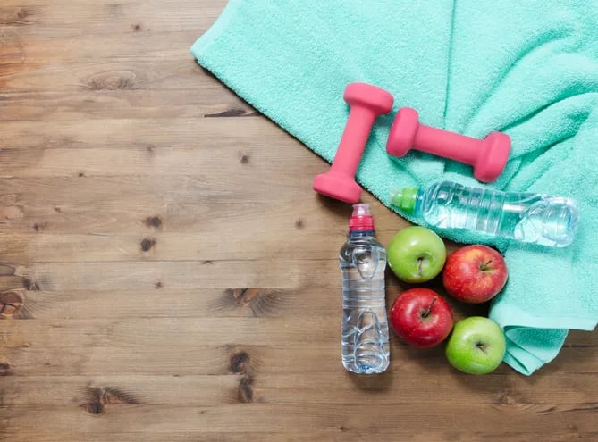 Una toalla sobre un piso de madera, con dos pesitas, dos botellas de agua, dos manzanas rojas y dos manzanas verdes.