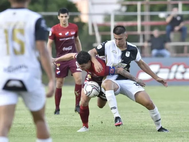 Juan Franco (rojo) de Nacional pelea por el balón con un futbolista de Tacuary en el partido de la séptima jornada del torneo Apertura 2022.
