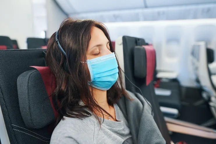 Una mujer con mascarilla viaja en un avión.