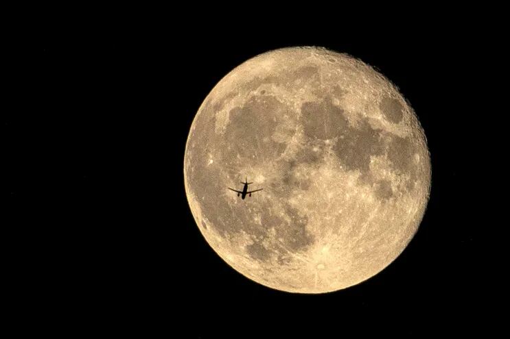 Un avión es visto desde la tierra, con la luna de fondo.