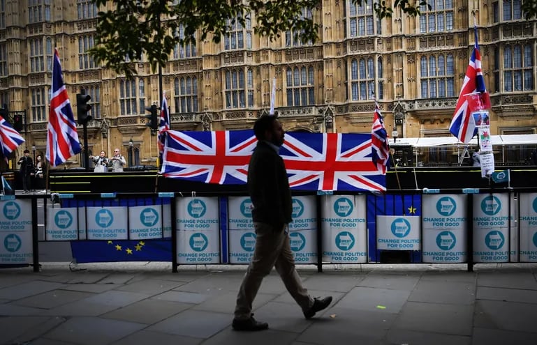 Un hombre camina frente a varias banderas del Reino Unido frente al Parlamento británico.