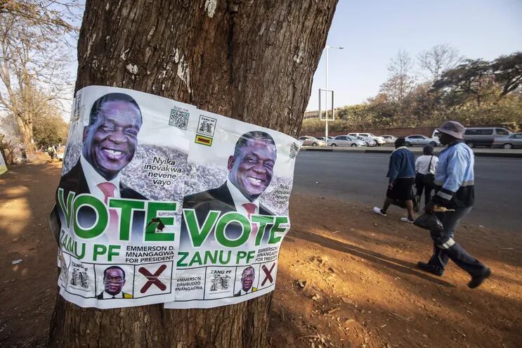 Ciudadanos caminan junto a carteles de la campaña electoral de 2023 de Emmerson Mnangagwa sobre un árbol en Harare, Zimbabue.