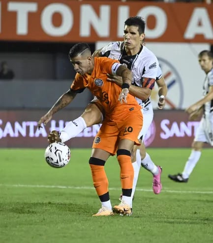 El delantero  Derlis  Alberto González (30 años) pone el cuerpo para cuidar el balón ante la rápida llegada del defensor Marcos Antonio  Cáceres (37). El “10” del Decano anotó el segundo gol, de penal.