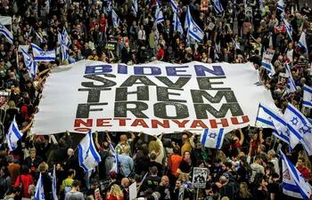 La gente levanta una gran pancarta pidiendo al presidente de los Estados Unidos que presione al gobierno israelí para que tome medidas para devolver a los rehenes mantenidos cautivos por militantes palestinos en la Franja de Gaza desde los ataques del 7 de octubre, durante una manifestación antigubernamental cerca de la sede del Ministerio de Defensa en Tel Aviv.