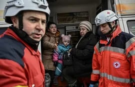 Miembros de la Cruz Roja Internacional ayudan en la evacuación de niños y mujeres en el oeste de Kiev, capital de Ucraniana. (AFP)