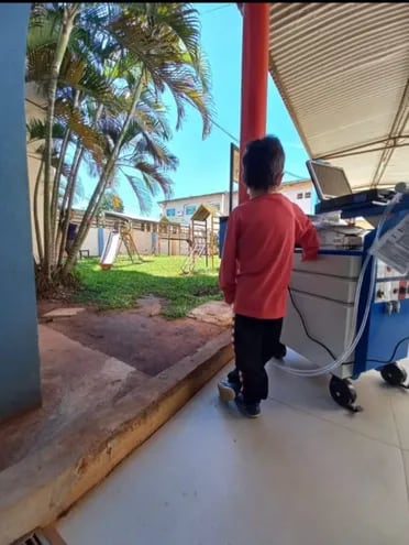Milan Alexander, de 5 años, observa el parque de diversiones del Hospital Pediátrico de Acosta Ñu, sujetándose de la máquina que lo mantiene con vida, su corazón artificial. Espera con fe a un donante para seguir viviendo y volver a jugar libremente.