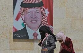 Dos mujeres caminan junto a un cartel con el retrato del rey Abdalá II de Jordania, en Amán.