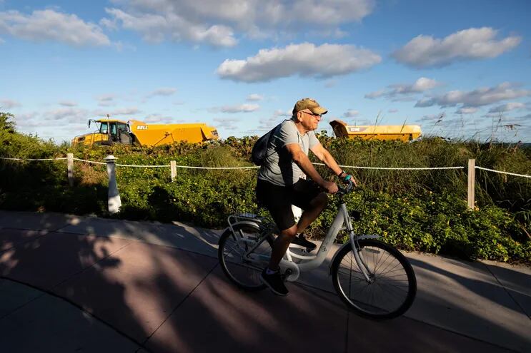 Un hombre pasea en bicicleta cerca de la maquinaria pesada usada para rellenar la costa de Miami Beach.