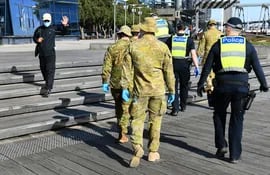 Un hombre saluda a un grupo de policías y soldados que patrullan el área de Docklands en Melbourne el 2 de agosto de 2020, después del anuncio de nuevas restricciones para frenar la propagación del coronavirus COVID-19.