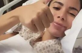 Anitta levantando el pulgar derecho en su cama de hospital, indicando que todo está bien.
