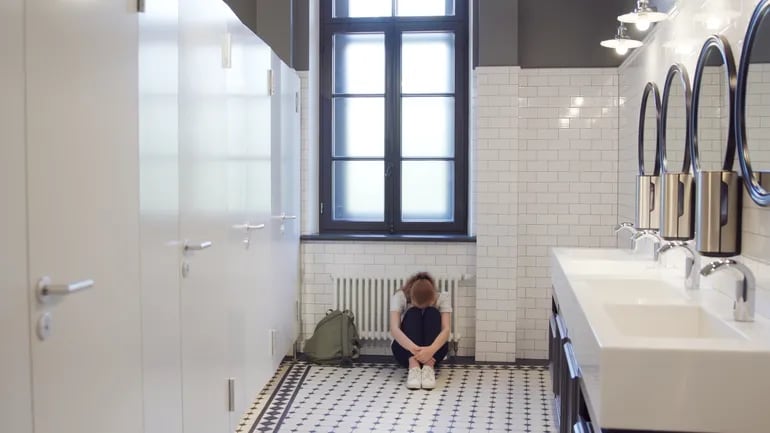 una alumna adolescente sentada en el piso del baño de su colegio