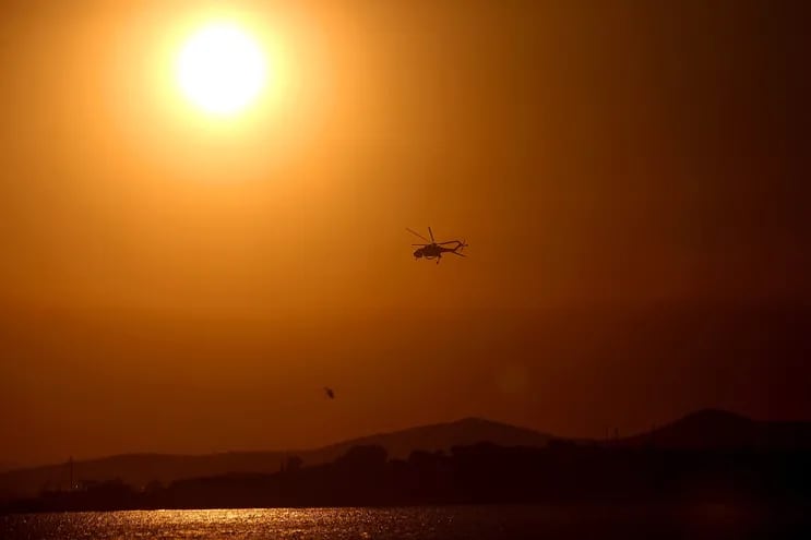 Un sol abrasador tiñe de naranja el cielo mientras helicópteros cargan agua para combatir un incendio forestal. La década concluida en 2023 fue la más cálida desde que hay  registros, según la ONU.