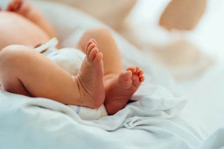 Pies de bebé recién nacido, con pañales, sobre una manta blanca.