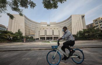 Un hombre pedalea su bicicleta frente a la sede del Banco Popular de China, en Pekín, China.