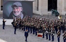 El presidente de Francia, Emmanuel Macron, camina frente a los miembros de la Guardia Republicana Francesa durante el acto de homenaje al actor Jean-Paul Belmondo, cuyo retrato es exhibido en una pantalla gigante.