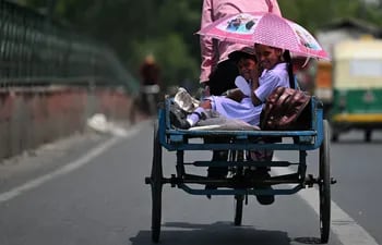 Los niños se refugian del sol bajo una sombrilla mientras viajan en la parte trasera de un carrito de bicicletas durante un caluroso día de verano en Nueva Delhi.