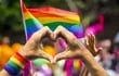 Imagen ilustrativa. Dos manos forman un corazón con banderas multicolores de fondo, en referencia a las uniones LGBTIQ+.