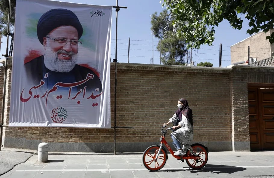 Una niña iraní pasea en bici por las calles de Teherán, donde pasa frente a un enorme cartel con el rostro del candidato presidencial conservador Ebrahim Raisi.