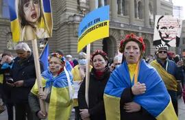 Manifestantes con banderas ucranianas cantan el himno nacional ucraniano durante una manifestación contra la invasión rusa frente al edificio del parlamento suizo en Berna, Suiza, el 19 de marzo de 2022.