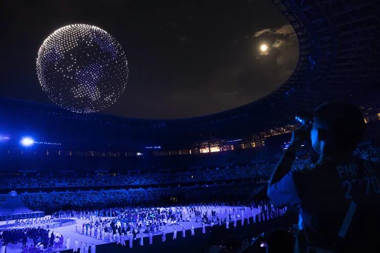 Un hombre fotografía los drones que forman un globo sobre el cielo durante la ceremonia de apertura de los Juegos Olímpicos Tokio 2020, en el estadio Olímpico de Tokio, Japón.