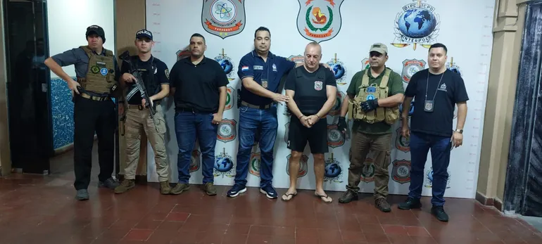 El italiano Gianni Casalini aparece esposado junto con los agentes de Interpol que participaron del operativo que derivó en su detención en San Lorenzo.