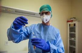 Un profesional de la salud con un traje protector y una máscara sostiene una muestra de coronavirus.