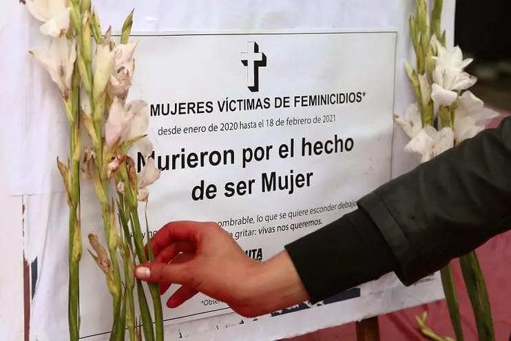 Una persona coloca una flor cerca de un cartel en honor a las víctimas de feminicidios.
