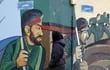 Una mujer camina frente a un mural que muestra a soldados de la Guardia Revolucionaria iraní, en Teherán.