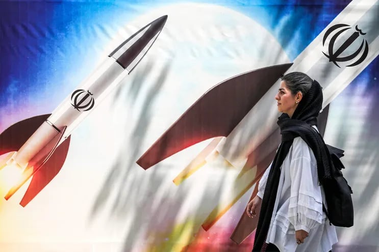 Una mujer camina frente a un mural que muestra misiles con el emblema de la República Islámica de Irán, en Teheran.