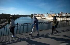La gente cruza el Puente de Triana en Sevilla el 2 de mayo de 2020, durante las horas permitidas por el gobierno para salir y hacer ejercicio, por primera vez desde el comienzo de un bloqueo nacional para prevenir la propagación de la enfermedad COVID-19.