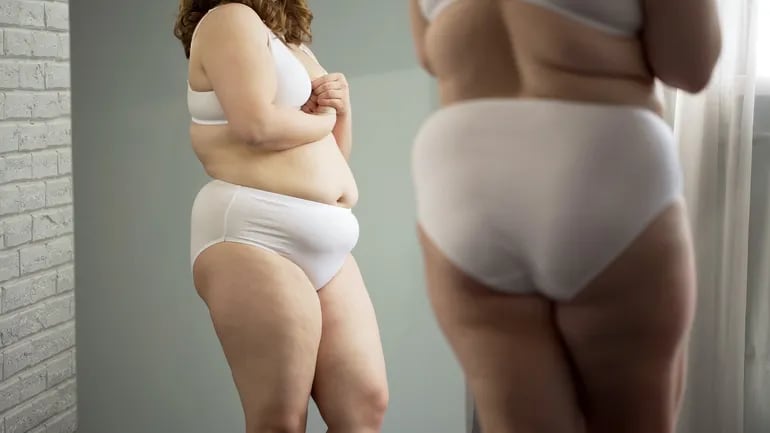 Una mujer con sobrepeso se mira al espejo.