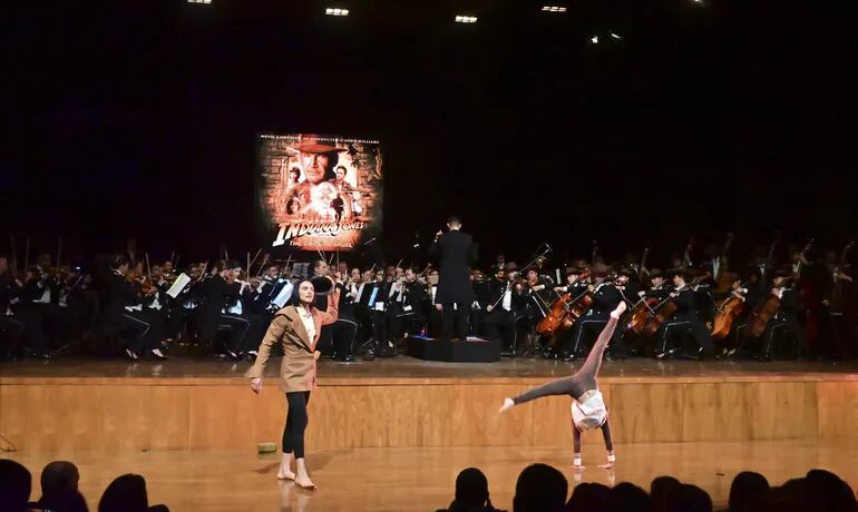La Orquesta Sinfónica de la Policía Nacional interpretando el tema de "Indiana Jones", junto a un par de acróbatas en el escenario.