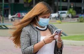 En Venezuela, una mujer con mascarilla camina con su teléfono celular en la mano.
