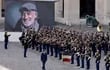 El presidente de Francia, Emmanuel Macron, camina frente a los miembros de la Guardia Republicana Francesa durante el acto de homenaje al actor Jean-Paul Belmondo, cuyo retrato es exhibido en una pantalla gigante.