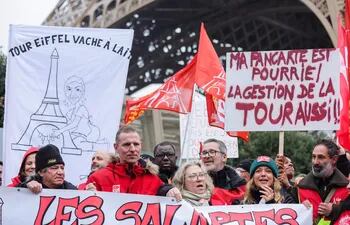 Los trabajadores en huelga llevan pancartas con los mensajes 'vaca lechera de la Torre Eiffel' (L) y 'mi pancarta es mala, también lo es la dirección de la torre' (R) durante una manifestación en Al pie de la Torre Eiffel en París.